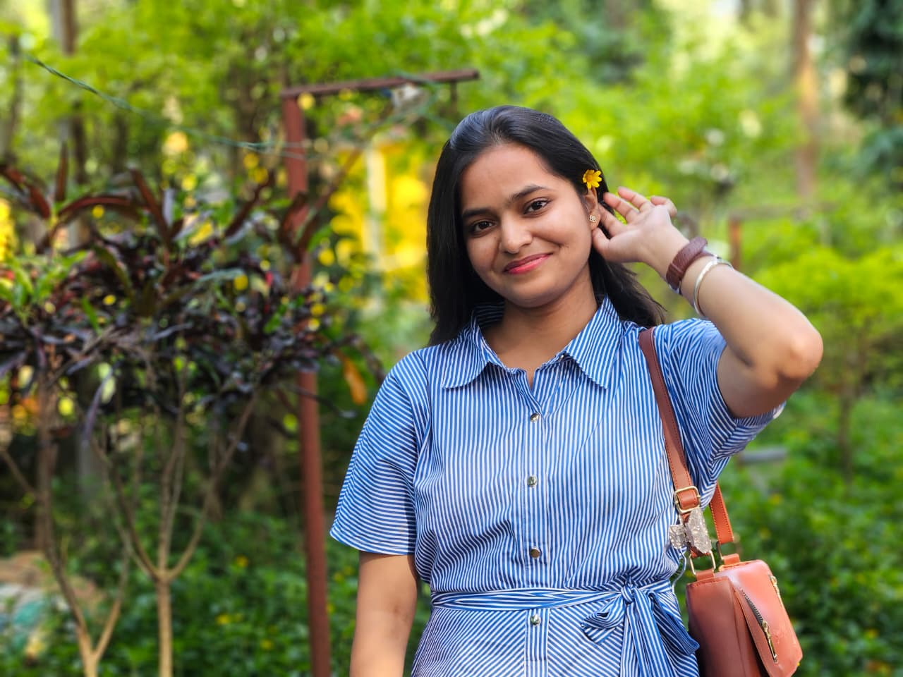 Subhashree wearing a blue striped dress with a yellow flower, in a green garden